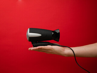 Male hand holding black hairdryer isolated on red background. Hirdresser salon, barber shop, household appliances store concept.