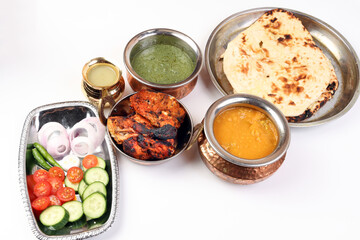 Spicy red Chicken grilled tikka tandoori nan bread green spinach curry yogurt sauce dal tomato cucumber onion salad set in metal stainless steel brass copper pot on white background