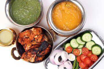 Spicy red Chicken grilled tikka tandoori nan bread green spinach curry yogurt sauce dal tomato cucumber onion salad set in metal stainless steel brass copper pot on white background