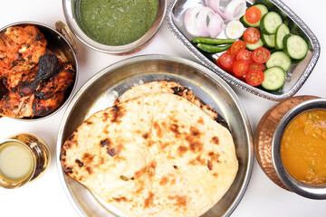 Spicy red Chicken grilled tikka tandoori nan bread green spinach curry yogurt sauce dal tomato cucumber onion salad set in metal stainless steel brass copper pot on white background