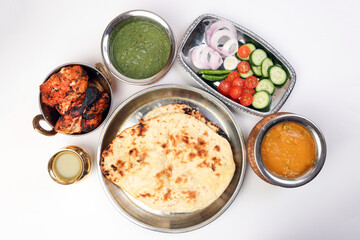 Spicy red Chicken grilled tikka tandoori nan bread green spinach curry yogurt sauce dal tomato cucumber onion salad set in metal stainless steel brass copper pot on white background