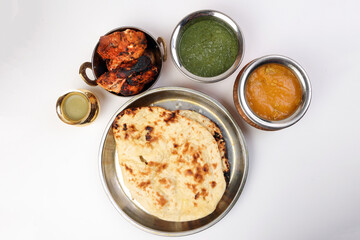 Spicy red Chicken grilled tikka tandoori nan bread green spinach curry yogurt sauce dal tomato cucumber onion salad set in metal stainless steel brass copper pot on white background