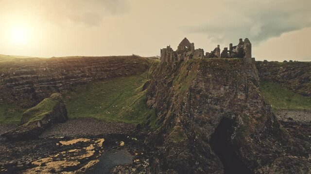 Dunluce castle ruins at sun sea bay aerial. Green basalt cliff at nobody nature landscape. Historic fortress at ocean seascape. Ancient architecture landmark in Antrim County, Northern Ireland, Europe