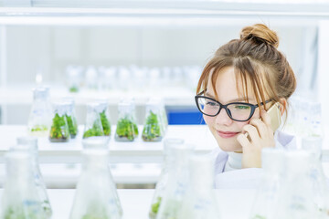 A girl laboratory assistant in a biological laboratory talking on the phone examining plants grown in a nutrient solution in flasks. Biological research at the university