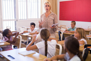 Portrait of professional female teacher giving lesson with interested tweens in primary school