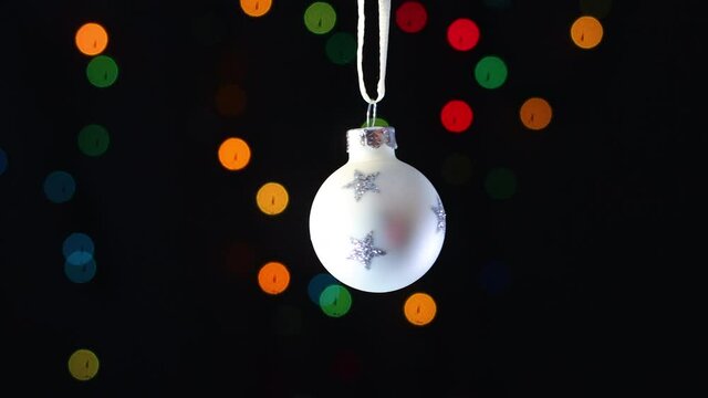 White Christmas ornament with glitter stars swing with blinking lights behind