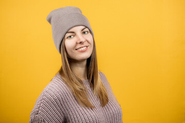 portrait of a smiling young woman. person dressed warm sweater and hat. isolated yellow background. copy space