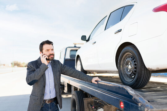 Male car owner on the phone and waiting for his ride next to a tow truck