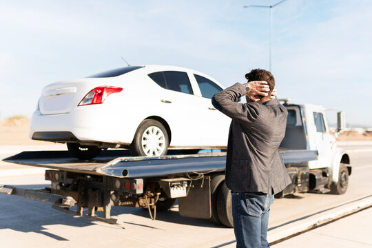 Rear view of an angry man watching his car on the tow truck