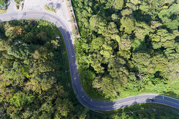 Aerial view drone shot top view of Asphalt road curve on mountain tropical rainforest with mountain peaks