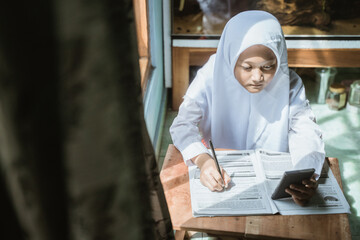 Fototapeta na wymiar indonesian schoolgirl studying homework during her online lesson at home, social distance during quarantine, online education concept, home schooler
