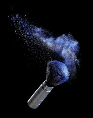 Blue powder splash and cosmetic brush for makeup on black background