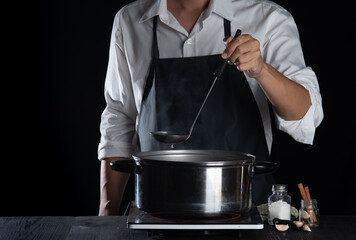 Man cooking soup in pot on dark background,Cooking at home