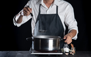 Man cooking soup in pot on dark background,Cooking at home