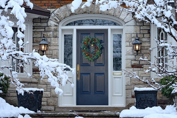 Front door in winter with seasonal wreath, surrounded by snow