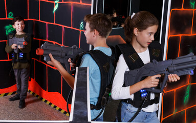 Portrait of excited sportive teen boy and girl aiming laser gun at other players during lasertag game in dark room