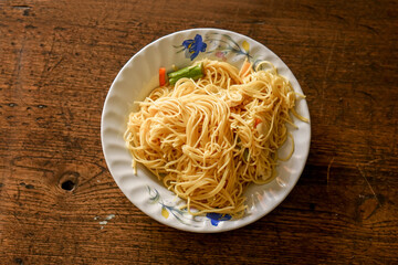 Closeup and top view fried Chinese noodle in white ceramic plate on wooden background. Thai and Chinese people popular eaten vegan foods in Chinese vegetarian festival in October every years