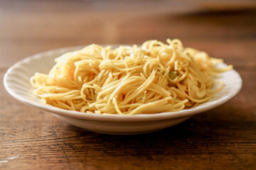 Closeup fried Chinese noodle in white ceramic plate on wooden and blurry background. Thai and Chinese people popular eaten vegan foods in Chinese vegetarian festival in October every years