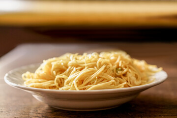 Closeup fried Chinese noodle in white ceramic plate on wooden and blurry background. Thai and Chinese people popular eaten vegan foods in Chinese vegetarian festival in October every years