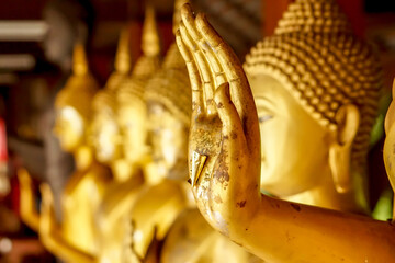 Closeup and crop hand of golden Buddha statue with a gold leaf on blurred golden Buddha statue stand strong line background