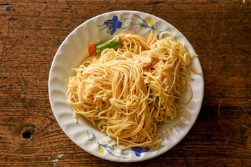 Closeup and top view fried Chinese noodle in white ceramic plate on wooden background. Thai and...