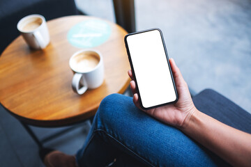 Mockup image of a woman holding mobile phone with blank white desktop screen with coffee cup on the table