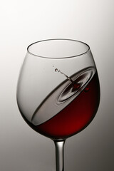 Glass with red wine and a drop of wine falling into the glass, on a white background
