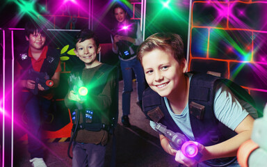 excited sportive young boy aiming laser gun at other players during lasertag game in dark room
