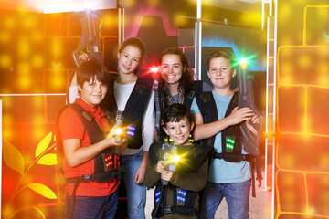 Smiling young woman and children with laser pistols posing together in dark laser tag labyrinth