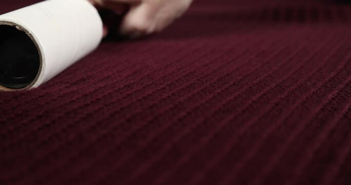  Close up macro view of a hand using a fabric roller perpendicular to the field of focus on a maroon sweater