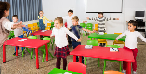 Portrait of children stretching with friendly female teacher during physical activity break in...