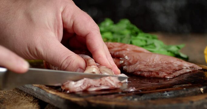 Men's hands cut with a raw squid knife on a cutting board. 