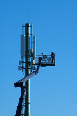 Telecommunications tower with 4G, 5G transmitters, Worker on cellular base station with transmitting antennas on a telecommunications tower against the blue sky