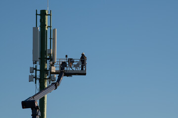 Telecommunications tower with 4G, 5G transmitters, Worker on cellular base station with transmitting antennas on a telecommunications tower against the blue sky