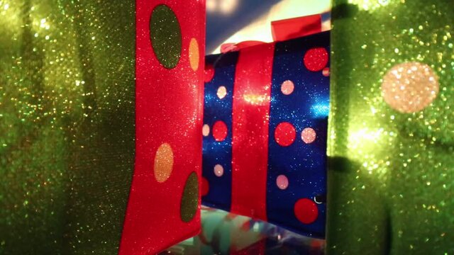 Passing between two red and green illuminated Christmas presents, moving towards a smaller red and blue present with a red bow on top positioned in the middle.