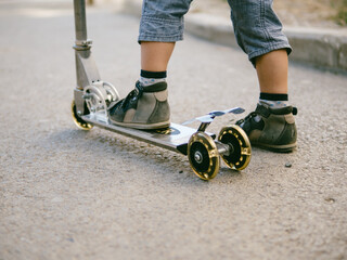 Fototapeta na wymiar Baby boy learn to skate on scooter. Close up view of small boy foot on kick scooter on asphalt. Copy space for text.