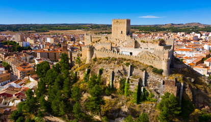 Fototapeta na wymiar Scenic aerial view of residential areas in small Spanish town of Almansa with dominating medieval walled Castle on hilltop on sunny fall day..