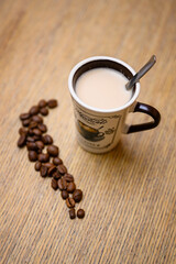 A small cup with coffee and a spoon and coffee beans lying next to it.
