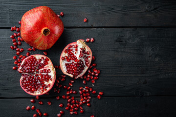 Ripe pomegranate with fresh juicy seeds, on black wooden table, top view with space for text
