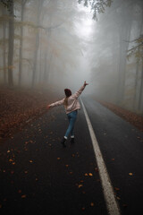 Fototapeta na wymiar Happy young woman on the road in beautiful autumn forest. Landscape with alone girl,orange trees. Empty roadway through foggy woodland in fall. 