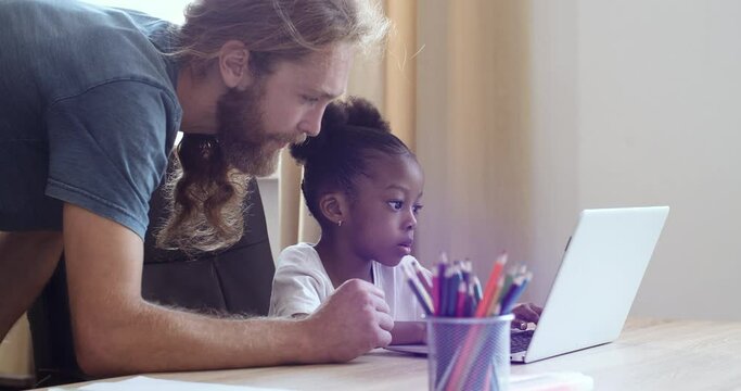 Multi ethnic family caucasian bearded young adult man father helping foster daughter afro american schoolgirl ethnic child with homework, home schooling concept e-learning during pandemic quarantine