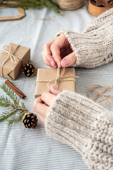 Natural Christmas background, craft gift boxes, cones, Christmas tree on the table, close-up, retro style. A girl in a sweater is packing gifts. The happy atmosphere of the holiday