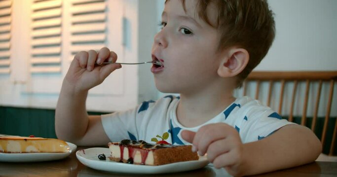 Cute healthy preschooler eating sweet cheesecake sitting in a children's cafe. At the restaurant Happy child eats a healthy organic cake with raspberry jam. Childhood, health and baby food concept.