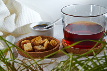 Square toasted pieces of homemade delicious rusk, hardtack, Dryasdust, zwieback, Liquid honey in a saucer and black tee in a cap on a white tablecloth.