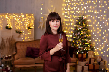 winter holidays concept - young beautiful woman drinking champagne in decorated living room with Christmas tree and festive led lights