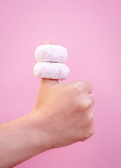 Two delicious donuts embedded in the thumb of a hand with a pink background.