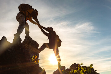 Silhouette Two Male hikers climbing up mountain cliff and one of them giving helping hand. People helping and, team work concept. - obrazy, fototapety, plakaty