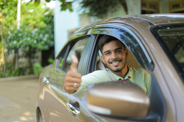 Young indian man sitting in new car and showing thumps up