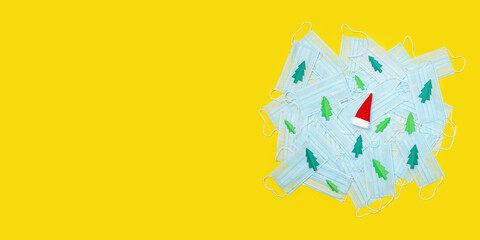 Medical protective masks against coronavirus, decorated with Christmas tree paper and Santa Claus hat. Flat lay, copy space. Coronavirus concept. Long wide banner