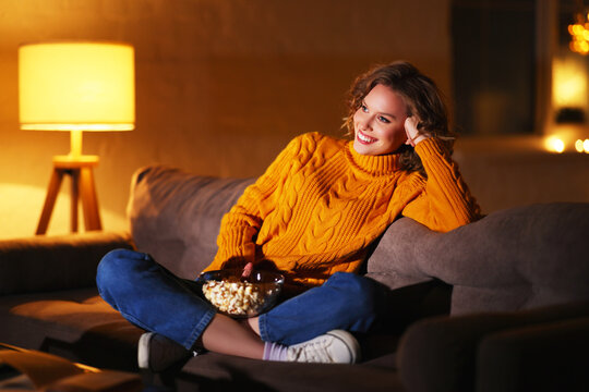 Positive woman with popcorn resting on sofa and watching TV.